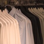Row of neatly hung dress shirts in white, light blue, and dark colors on a clothing rack.